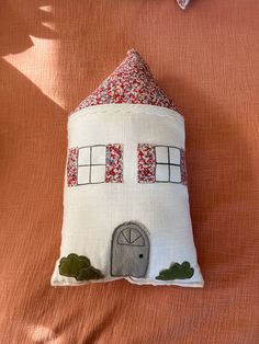 a decorative pillow with a house made out of fabric on top of an orange sheet