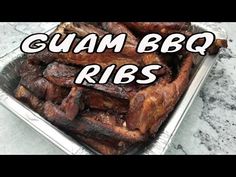 there is a metal tray with ribs in it on the marble counter top that says guam ribs