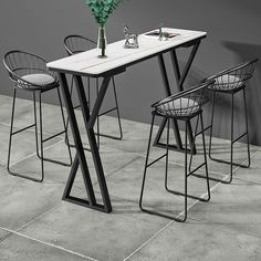 a table with four chairs and a vase on it, sitting in front of a gray wall