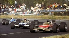 two racing cars driving down a race track with spectators in the stands behind them and onlookers watching