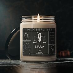 a candle with zodiac signs on it sitting on a table next to a black mug