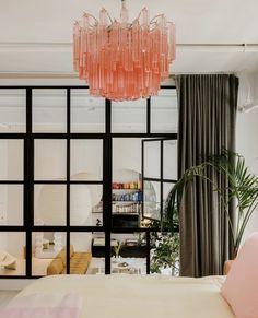 a pink chandelier hangs from the ceiling above a bed in front of a window