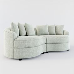 a white sectional couch with pillows on the top and bottom corner, in front of a gray background