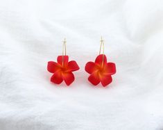 two red flower shaped earrings sitting on top of a white sheet