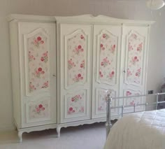 a white armoire with pink flowers painted on the doors and bottom panel, in a bedroom