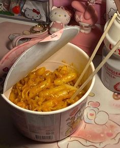 a bowl filled with macaroni and cheese next to a hello kitty doll on the table