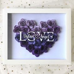 a white frame with purple paper flowers in the shape of a heart