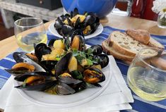 two plates of mussels on a table with bread and wine glasses next to them