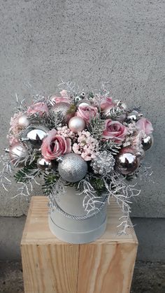 a vase filled with pink roses and silver ornaments on top of a wooden block in front of a concrete wall