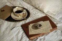 a cup of coffee sitting on top of a bed next to an old fashioned book