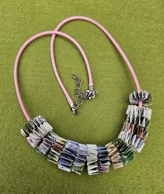 a necklace made out of magazines is laying on the ground next to a pink cord