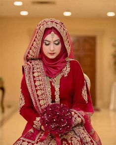 a woman in a red and gold bridal gown sitting on a chair with flowers