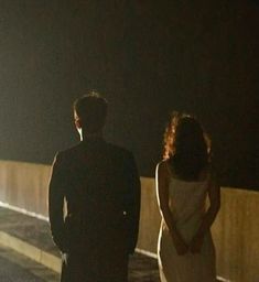 a man and woman standing next to each other on a bridge in the night time