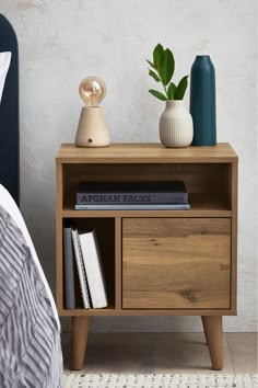 a nightstand with books and vases on top of it next to a blue bed