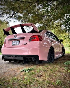 the back end of a pink car parked in front of a tree