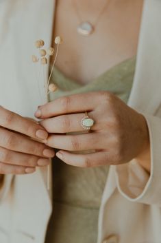 a woman wearing a white jacket and holding a flower in her left hand with one ring on it