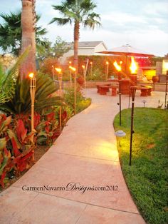 a pathway leading to some tables and umbrellas in the evening with lights on them