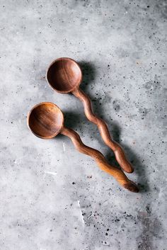 two wooden spoons sitting next to each other on top of a cement floor,