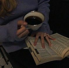 a woman holding a cup of coffee while reading a book