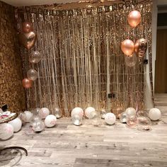 balloons and streamers are hanging from the ceiling in front of a backdrop with gold, white and pink balls