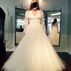 a woman standing in front of a mirror wearing a white wedding dress with long sleeves