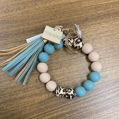 a blue and white beaded bracelet with tassels on a wooden table next to a keychain