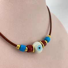 Evil eye necklace with colorful beads and leather cord to protect women. Great for the glass jewelry lover, blue eye, and minimalist jewelry.  Suitable as a choker but also an extender chain available.  Leather cord is in brown tones, white, red, and green handmade oval glass beads, gold materials, gold closure, and gold chain extension. Length of necklace (end to end on a flat surface): 19'' (49 cm) Size of inline beads part: 3'' The necklace is produced individually and is a unique product for you. It is made of the highest quality materials; it does not tarnish in any way. Women Protection, Colorful Beaded Necklace, Cord Choker, Necklace Colorful, Jewelry Accessories Ideas, Protection Necklace, Summer Gifts, Brown Tones, Blue Eye