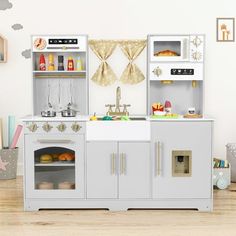 a play kitchen with white cabinets and silver appliances in a child's play room