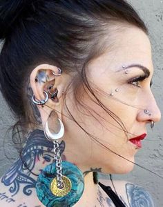 a woman with tattoos and piercings on her neck is looking at the camera while wearing an ear chain