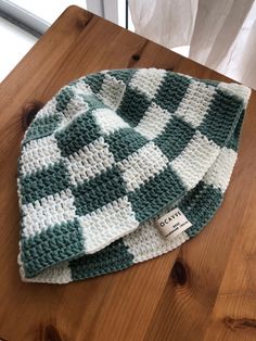 a green and white crocheted beanie sitting on top of a wooden table