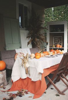 an outdoor table set for two with pumpkins and gourds on the table