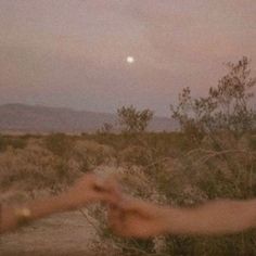 two people reaching out their hands to touch each other in the desert at night time