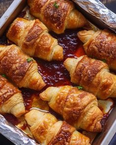 several croissants wrapped in tin foil sitting on top of a pan filled with sauce