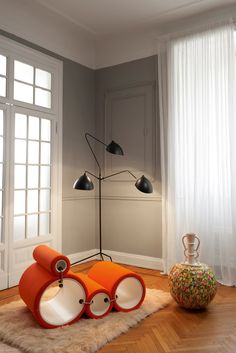 an orange chair sitting on top of a wooden floor next to a lamp and window