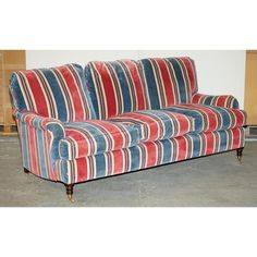 a red, white and blue striped couch sitting on top of a cement floor next to a wall