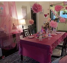 a dining room table covered in pink tissue pom poms and paper flowers with other decorations