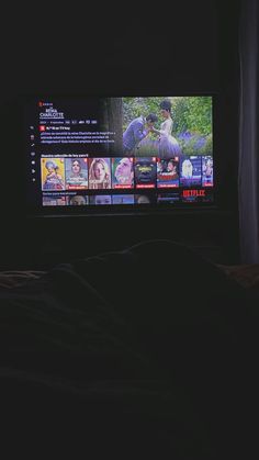 a flat screen tv sitting on top of a bed in a dark room next to a window