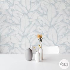 two vases with flowers in front of a wallpapered background that looks like leaves