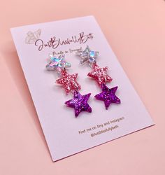 two pink and purple star earrings on top of a card