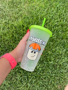 a hand holding a green cup with an orange helmet on it, in the grass