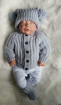 a baby doll wearing a knitted hat and sweater laying on top of a white blanket