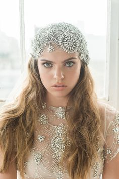 a woman with long hair wearing a veil and headpiece in front of a window