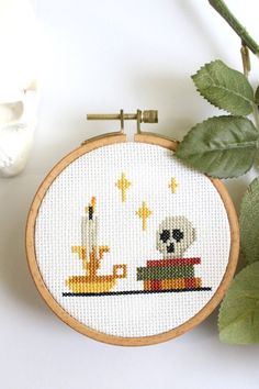 the cross stitch pattern is on display next to some leaves and a vase with flowers