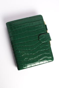 a green notebook with a gold ring on the front cover and an alligator embossed pattern