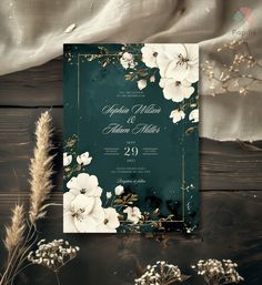 an elegant wedding card with white flowers and greenery on the front, in teal green