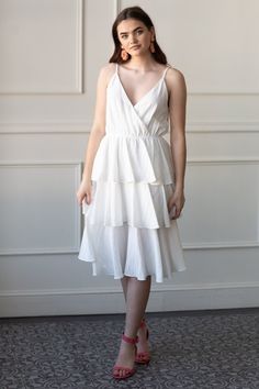 a woman standing in front of a wall wearing a white dress