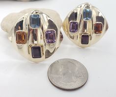 Title: Multicolor Gemstones Round Corner Square 14KT Yellow Gold Omega Clip Earrings Designer: Unbranded Material14KT Stamped Style: Vintage Gemstone Details All measurements are approximate and may vary slightly from the listed dimensions.1ar Approximately 5mm x 4mm each 1Amethyst Rectangular 1 Blue Topaz Rectangular 1 Orange Citrine Rectangular 1 Garnet Rectangular Estimated Measurements of the item30.23mm x 20.23mm x 5.83mm Estimated Total Weight of the Item DWT: 7.6 Grams: 11.7 Condition: Pr Luxury Multicolor Earrings With Gemstone Accents, Luxury Multi-stone Gold Earrings, Modern Multi-stone Yellow Gold Earrings, Modern Yellow Gold Multi-stone Earrings, Gold Oval Multi-stone Earrings, Oval Gold Multi-stone Earrings, Multicolor Gemstone Accented Earrings For Formal Occasions, Modern Gold Multi-stone Gemstones, Luxury Gold Earrings With Stones