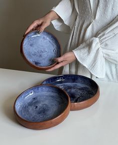 a woman is holding two blue bowls on a white counter top, with one bowl in the shape of a moon