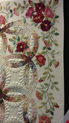 a close up of a quilted wall hanging with flowers and leaves on the border