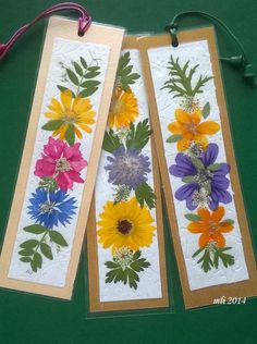 three bookmarks with colorful flowers on them hanging from a string next to each other